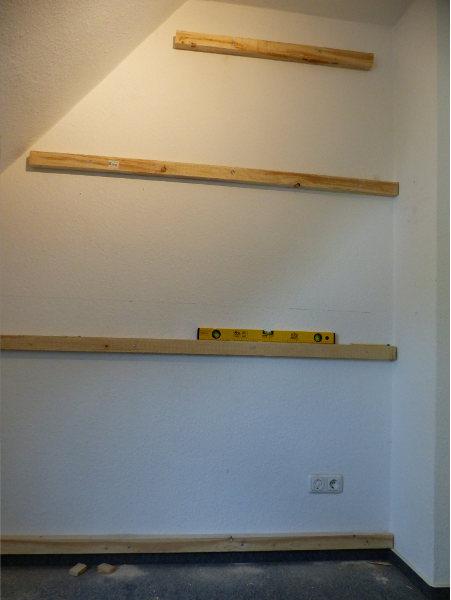 Mithilfe einer Wasserwaage und Schrauben werden die Holzlatten an der Wand befestigt.