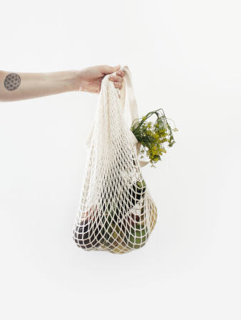 Detailaufnahme einer Hand, die ein Einkaufsnetz mit Gemüse hält.