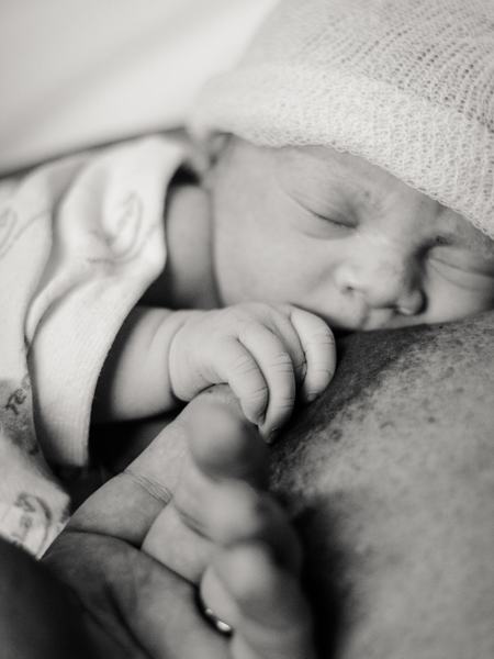 Detailaufnahme eines Neugeborenen an der Brust mit geschlossenen Augen.