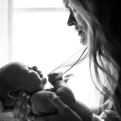 Eine Mutter hält ihr Baby im Arm und schaut es an. Es ist ein Schwarzweiß-Foto.
