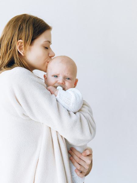 Aufnahme einer Frau mit einem Baby mit Schnuller auf dem Arm, welches traurig wirkt.