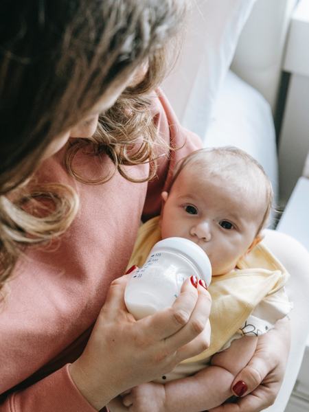 Aufnahme eines Babys, welches von einer Frau mit der Flasche geüttert wird.