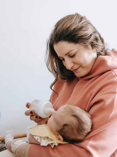 Eine Frau hält eine Babyflasche vor das Gesicht eines Babys.