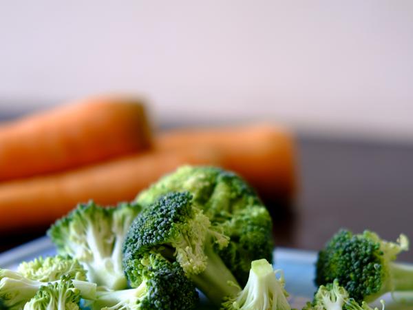 Etwas Gemüsen. Ein Brokoli liegt zerteilt im Fokus. Im Hintergrund sieht man Möhren.