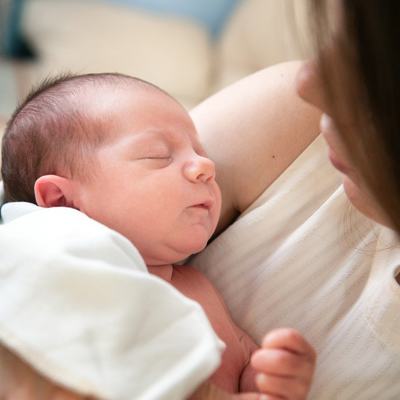 Ein Säugling wird von seiner Mutter auf dem Arm gehalten während sie es beim Schlafen beobachtet