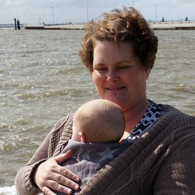 Ein Foto von Anna, wie sie ihren Sohn im HopTye trägt. Im Hintergrund ist das Meer zu sehen.
