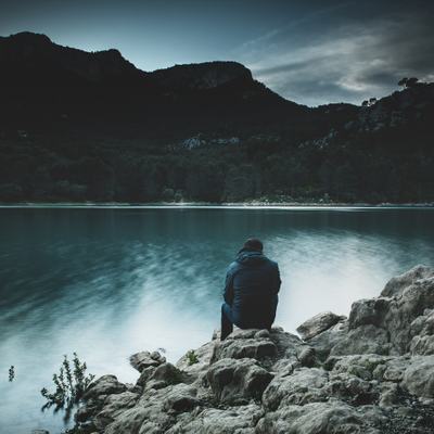 Eine Person sitzt mit einer Winterjacke an einem ruhigen See.