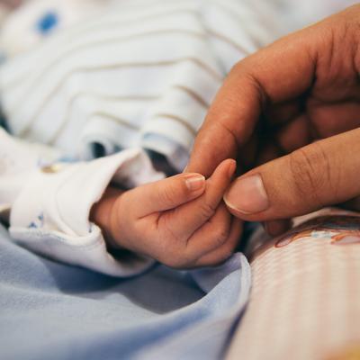 Die Hand einer Mutter hält den Finger ihres Neugeborenen.