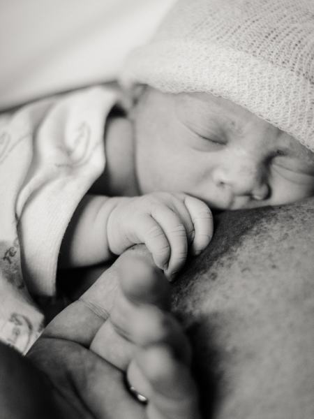 Aufnahme eines Baby an einer Brust, wobei die Hand des Babys einen Finger hält.