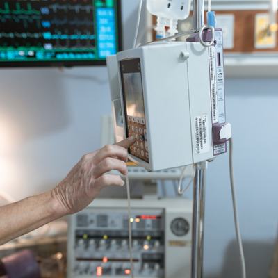Eine Hand bediehnt ein Messgerät in einem Krankenhauszimmer.