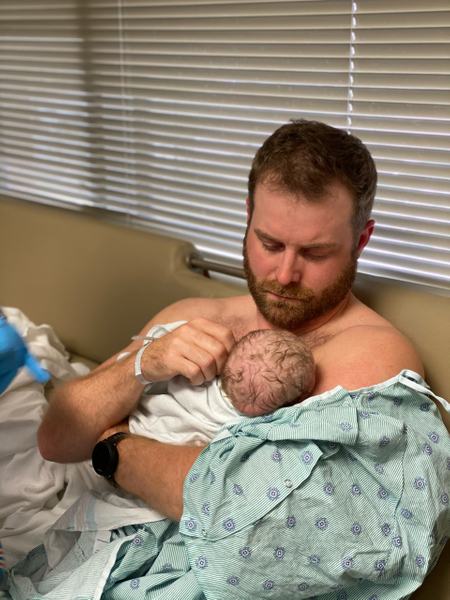 Aufnahme eines sitzenden Mannes, welcher ein Baby auf dem Arm hält.