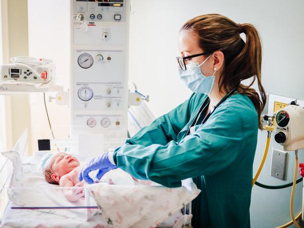 Aufnahme einer Frau, welche ein Baby inmitten medizinischer Gerät zu versorgen scheint.