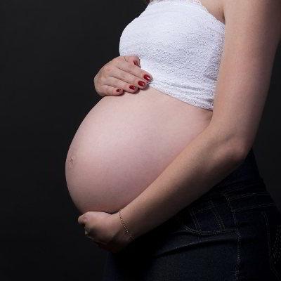 Ein Babybauch. Die schwangere Frau hält ihren Bauch mit beiden Händen fest.