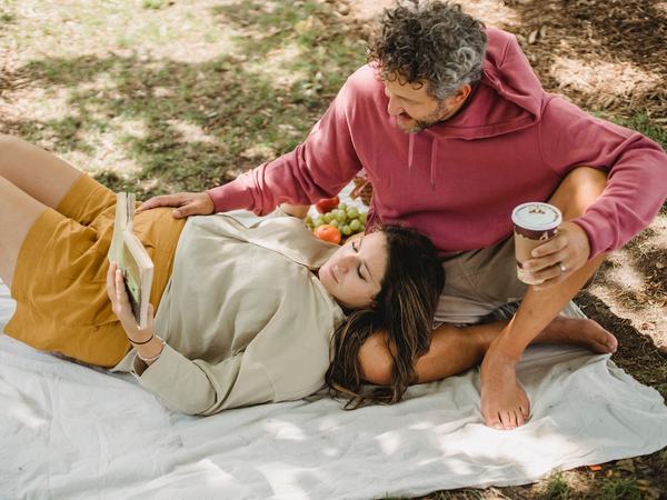 Aufnahme eines schwangeren Paares auf einer Picknickdecke, wobei die Frau ein Buch in der Hand hält.