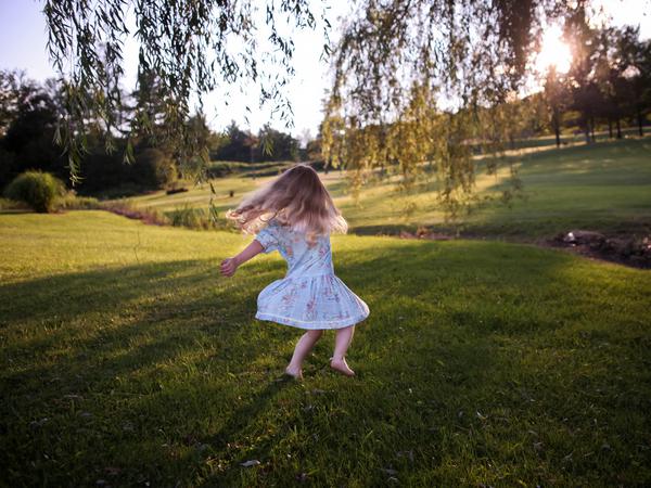 Ein Kind in einem Kleid springt fröhlich auf einer Wiese in die Luft.