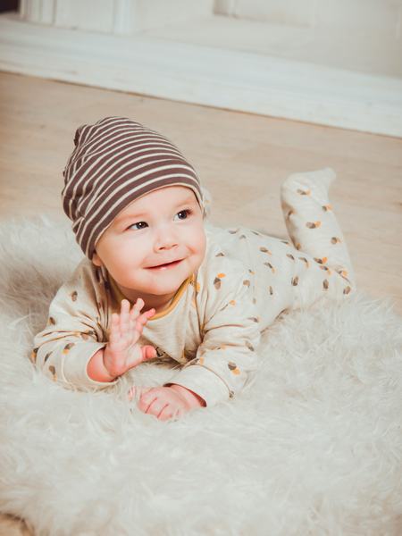 Ein auf dem Boden liegendes Baby lächelt und winkt.