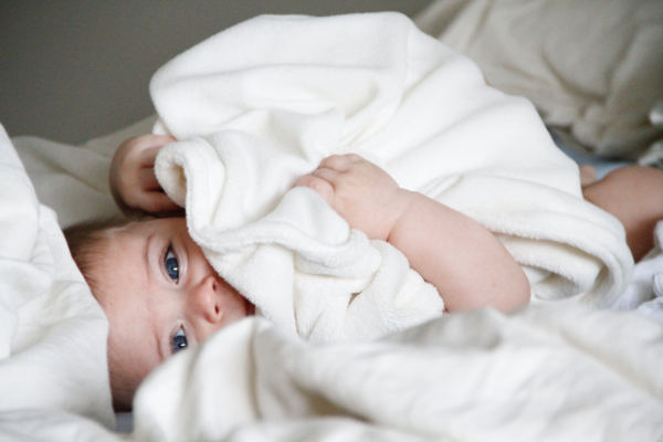 Ein blauäugiges Baby ist in eine weiße Decke gekuschelt.