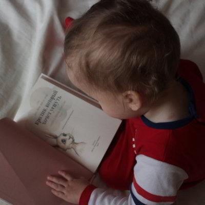 Ein Kind in einem roten Strampler schaut sich ein Buch mit einem Kaninchen an.