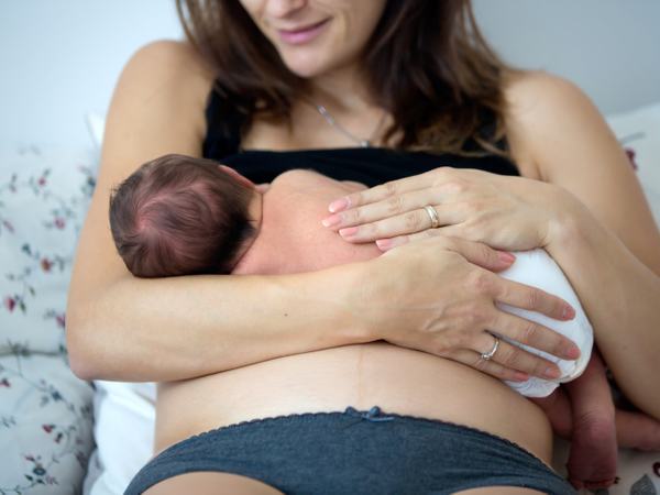 Eine Baby liegt auf dem Bauch einer Frau und scheint zu stillen.