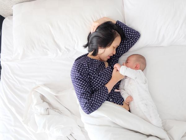 Aufnahme einer Frau im Bett liegend nah bei einem Baby.