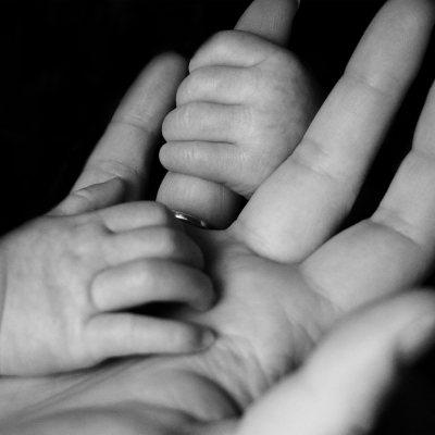 Schwarz-Weiß-Foto einer Kinderhand, die nach der Hand der Mutter greift.