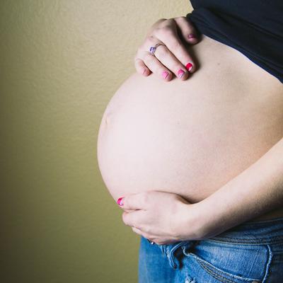 Eine schwangere Frau streicht sich über den Babybauch.