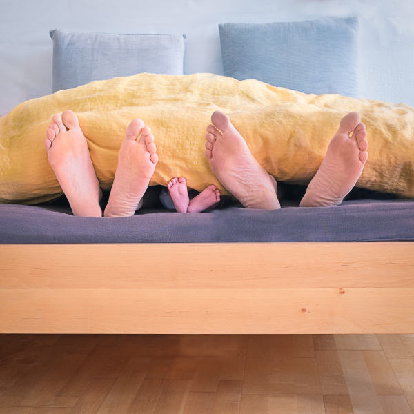 Eine Familie Schläft unter einer Decke. MAn sieht nur die Füße.