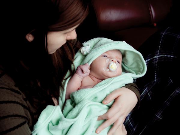 Ein in ein Handtuch gewickeltes Baby hält einen Schnuller im Mund.
