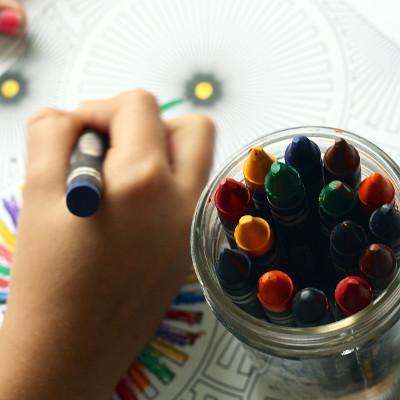 Eine Kinderhand die mit Wachsmalstiften malt.