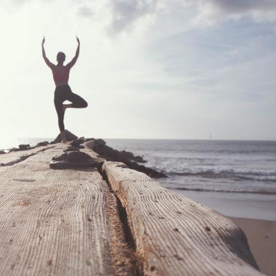 Aufnahme einer Frau, die auf einem Steg am Meer Yoga-Übungen macht.