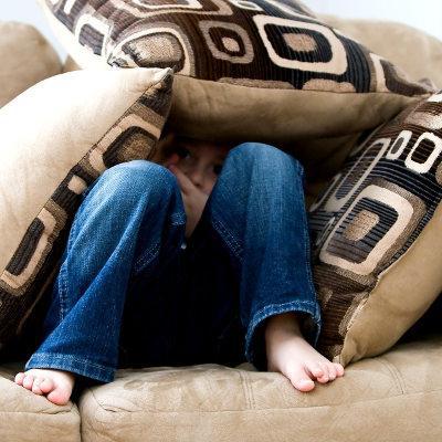 Ein ängstliches Kind versteckt sich in einem Berg aus Kissen, während es auf dem Sofa sitzt.