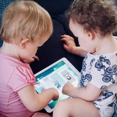 Zwei Kinder schauen sich gemeinsam ein Tablet an und scheinen in Interaktion miteinander.