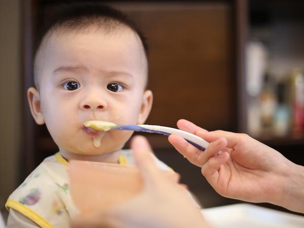 Foto eines Baby, welches einen Löffel mit Brei in den Mund gesteckt bekommt.