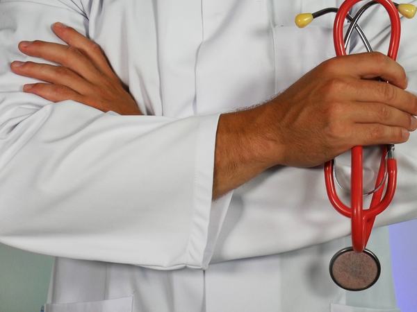 Detailaufnahme eines Mannes in weißem Arztkittel mit Stethoskop in der Hand.