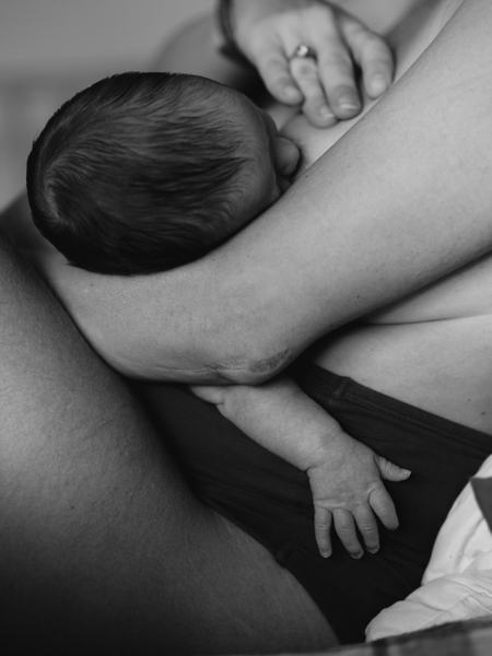 Teilaufnahme eines Baby, welches in der Wiegeposition gestillt. Die Frau hält dabei ihre Brust.