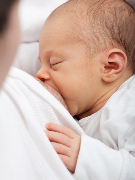 Teilaufnahme eines stillenden Babys mit geschlossenen Augen.