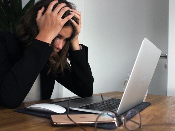 Teilaufnahme einer Frau, welche ihren Kopf auf ihre Hände stützt und vor einem Laptop sitzt.