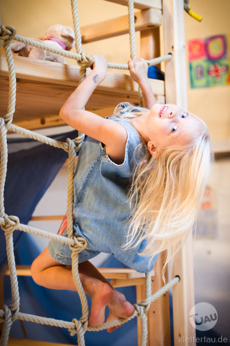 Ein Kind mit langen Haaren klettert an einem Kletternetz.