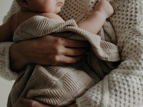 Ein in eine Decke gehülltes Baby wird auf dem Arm gehalten.