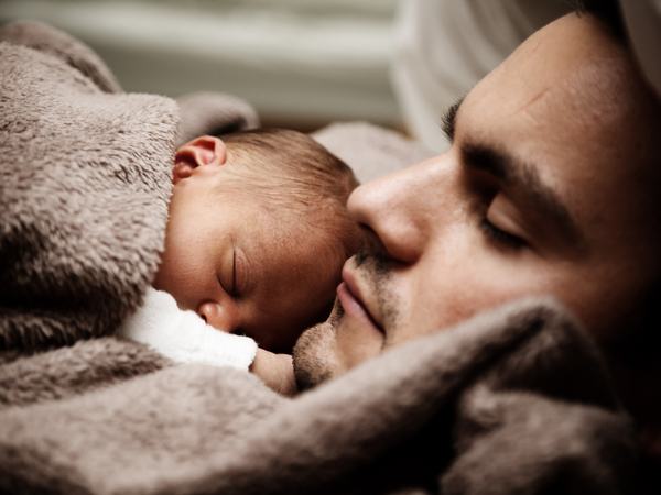 Ein Baby schläft liegend auf einem Mann, vermutlich seinem Papa.