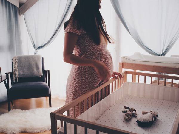 Eine schwangere Frau steht vor einem Babybett.