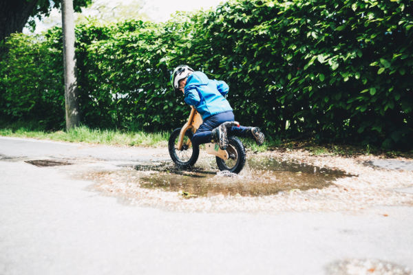 Ein Kind auf einem Laufrad fährt durch eine Pfütze.