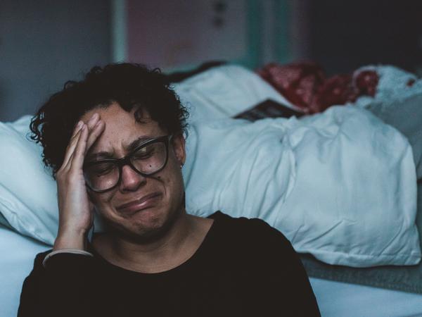 Eine Frau sitzt weinend vor einem Bett.