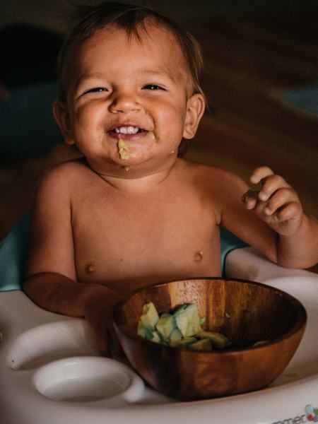 Aufnahme eines Baby, welches am Tisch mit Essen sitzt.