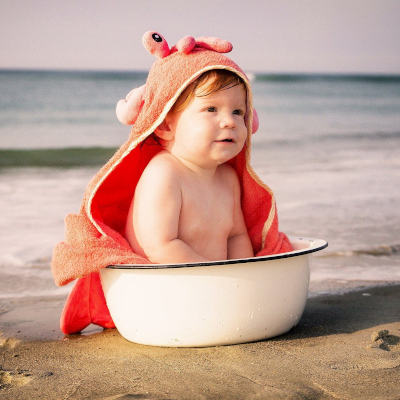 Ein Kleinkind sitzt in ein Handtuch gewickelt am Meer in einer Wanne.