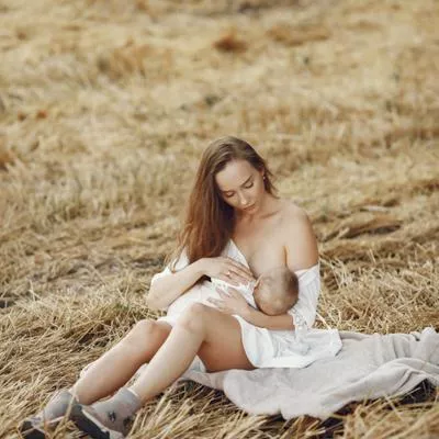 Eine Mutter stillt ihr Baby in einem weißen Kleid auf einer Wiese.